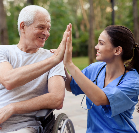 Personal médico chocando los cinco con un hombre adulto en silla de ruedas.