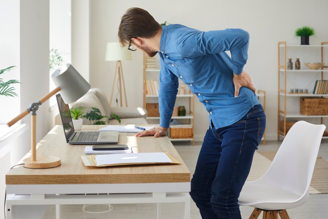 Hombre cansado siente espasmo e intenso dolor de espalda al levantarse después de trabajar con el ordenador en postura sedentaria durante mucho tiempo. Empleado joven infeliz y estresado tiene radiculitis o inflamación del nervio pinzado