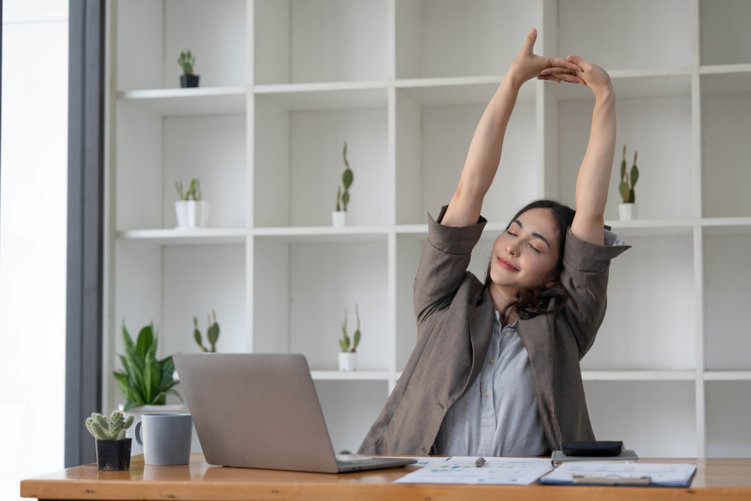 Asian businesswoman stretches her arms to relax her tired muscles from working at her desk all day at the office.