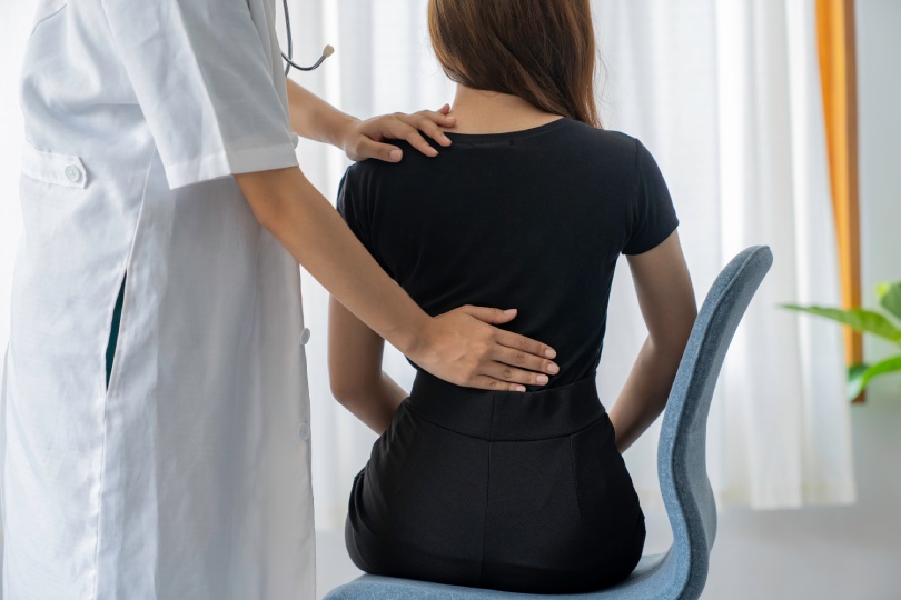 Mujer médico haciendo fisioterapia para tratar la espalda. Mujer oficinista tratamiento dolor espalda. Médico, quiropráctico, síndrome de oficina.