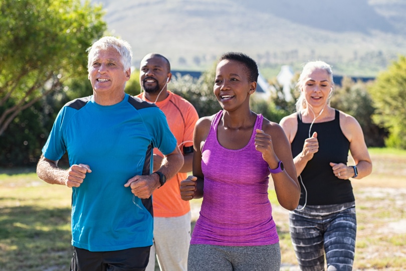 Grupo sano de personas maduras haciendo footing en la pista de un parque. Pareja mayor feliz corriendo en el parque con amigos africanos. Amigos multiétnicos de mediana edad haciendo ejercicio juntos al aire libre.