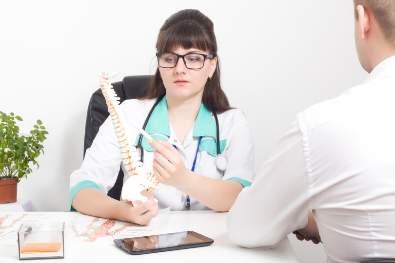 The doctor explains to the patient on the layout of the spine how the modern surgery on the wound will be performed laser puncture for protrusion and herniated discs, deformities