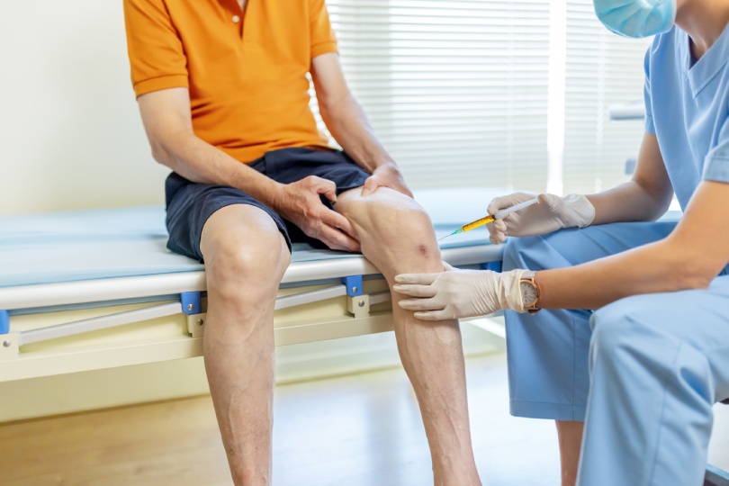 close up of asian female doctor make injection to male elderly senior patient in knee at hospital