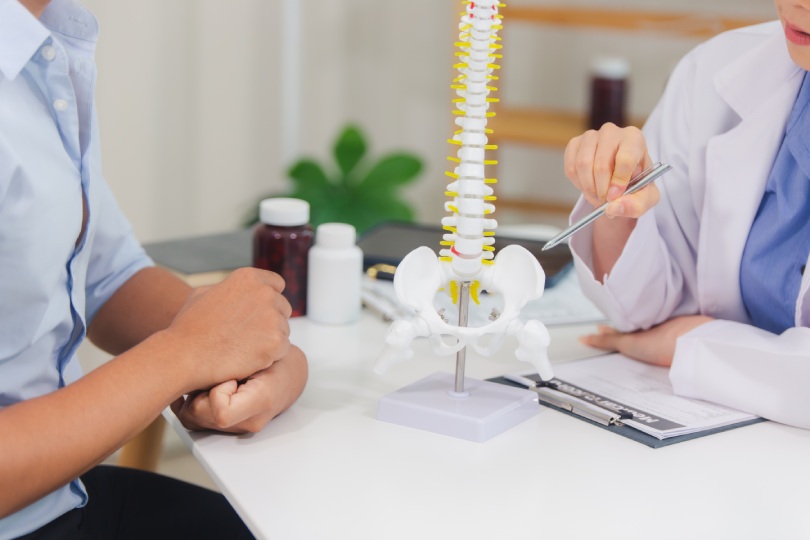 An orthopedic doctor shows a spinal model to a patient in a human spinal hospital. Diseases and disorders of the spinal cord, back pain, lumbar pain, orthopedic surgery, chiropractic, office syndrome