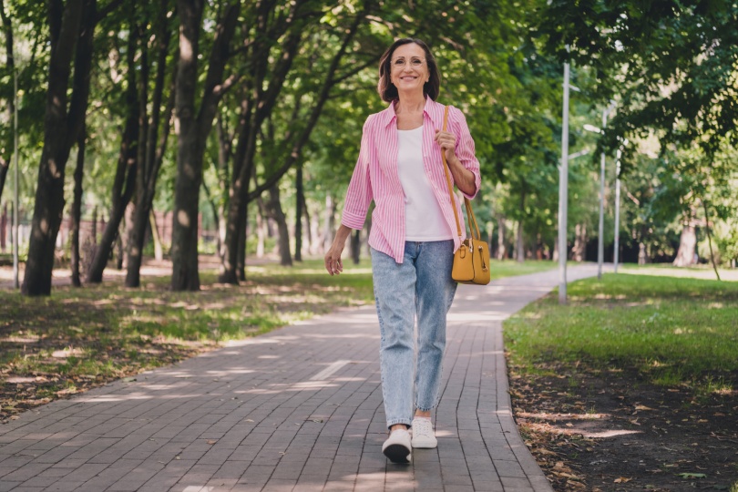 Foto de bonita y adorable señora pensionista llevar camisa rosa caminando sonriendo al aire libre campo jardín